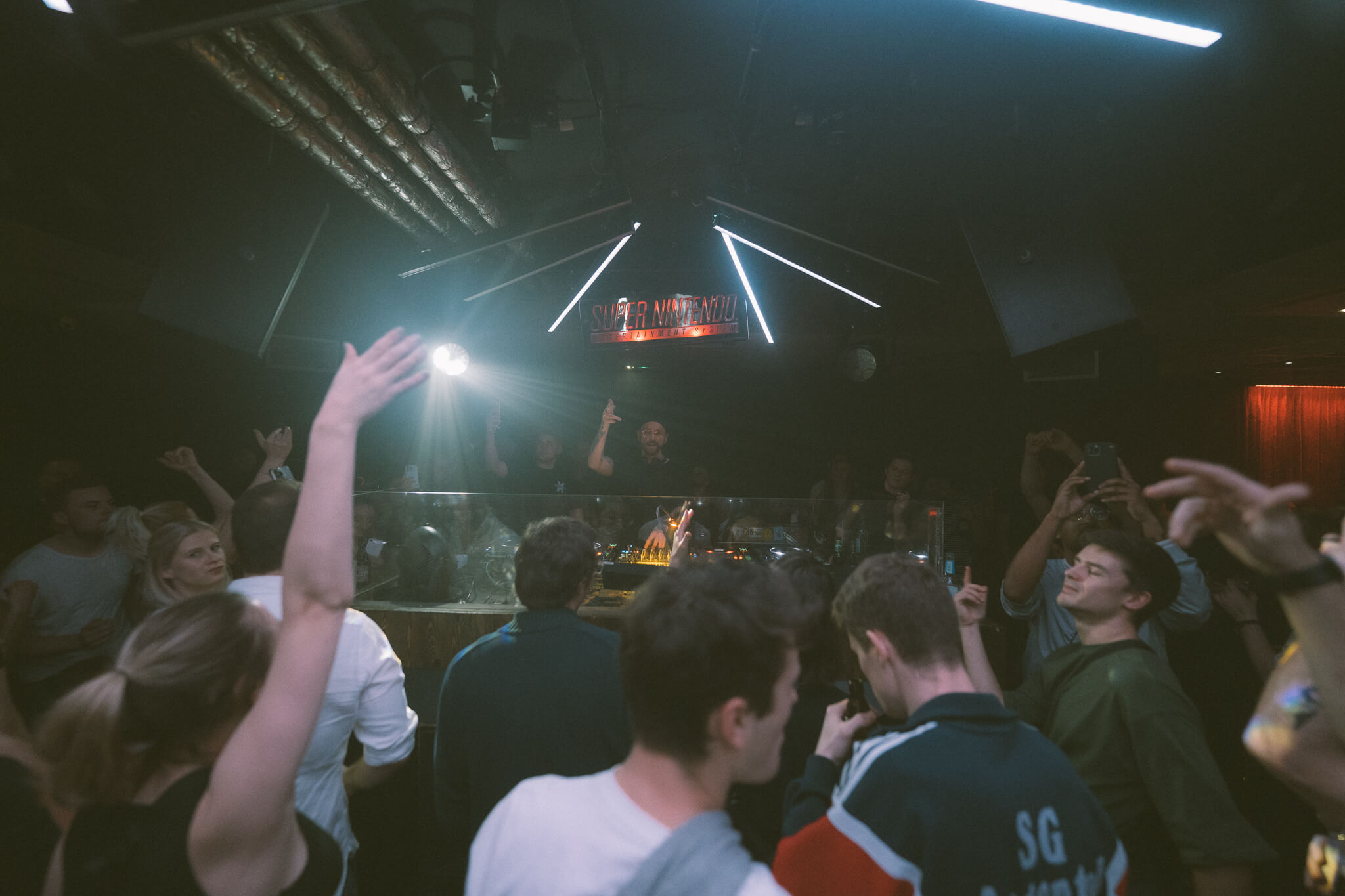 Eine Menschenmenge steht in einem Club vor einem DJ und feiert zu electro musik