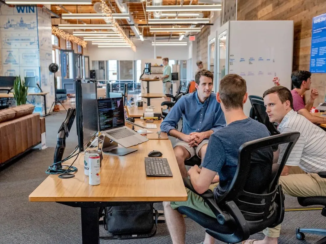 Three coworkers sitting around a desk with a computer setup in an office.