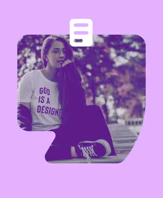 Uma jovem sentada em um banco, usando uma camiseta branca com a frase "GOD IS A DESIGNER", com um fundo de árvores desfocado.