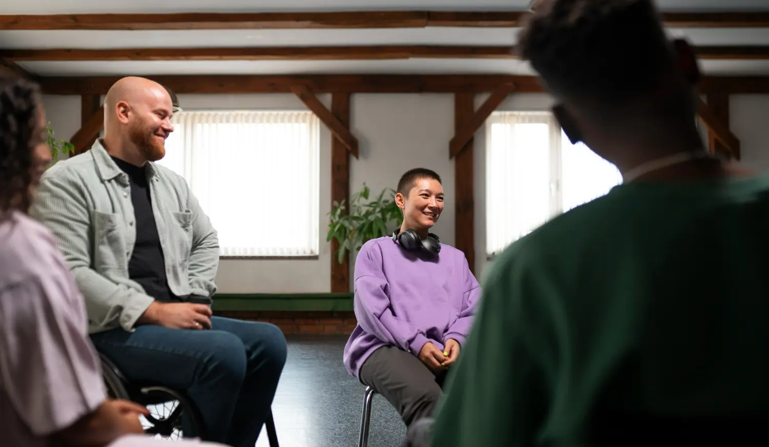 People sitting in a small group session, smiling and talking together in a bright room—showing connection, support, and community within an alumni program