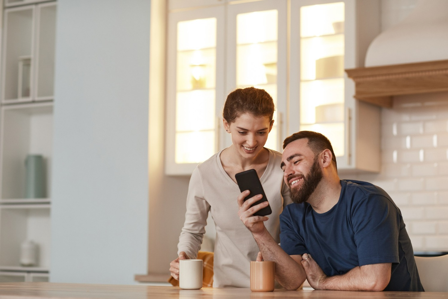 Smiling couple in a kitchen looking at a smartphone together, representing easy and secure alumni communication through a recovery app