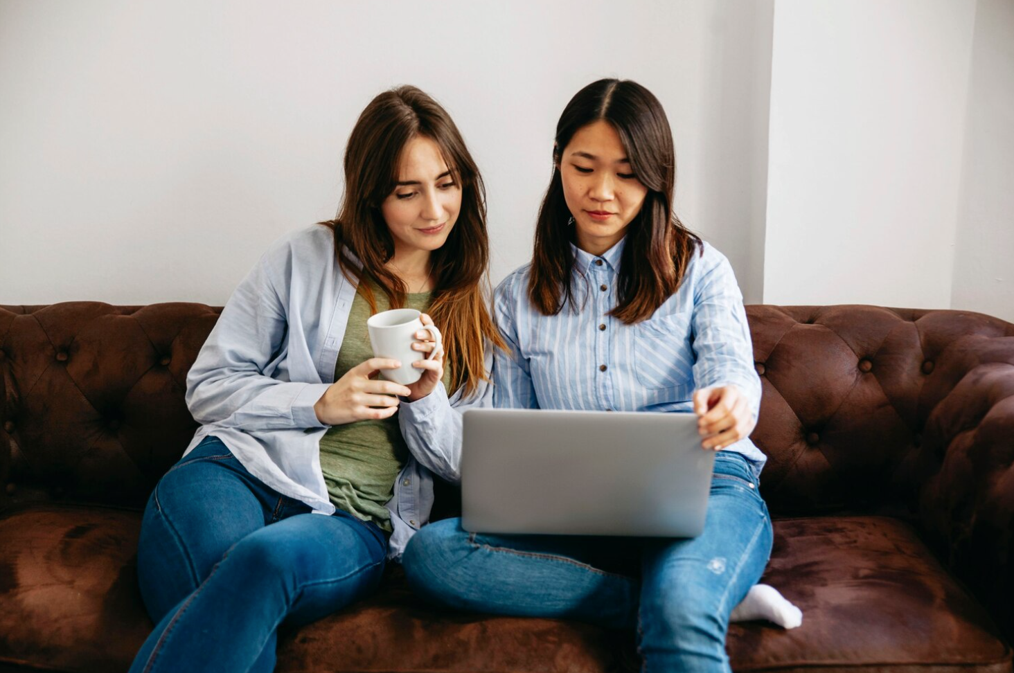 Two women sitting on a couch, focused on a laptop, engaged in a discussion about behavioral health alumni management 