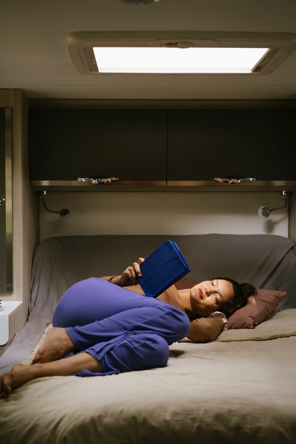 Freelance no-code Webflow developer Magda lying down in a camper van's bed reading her e-book