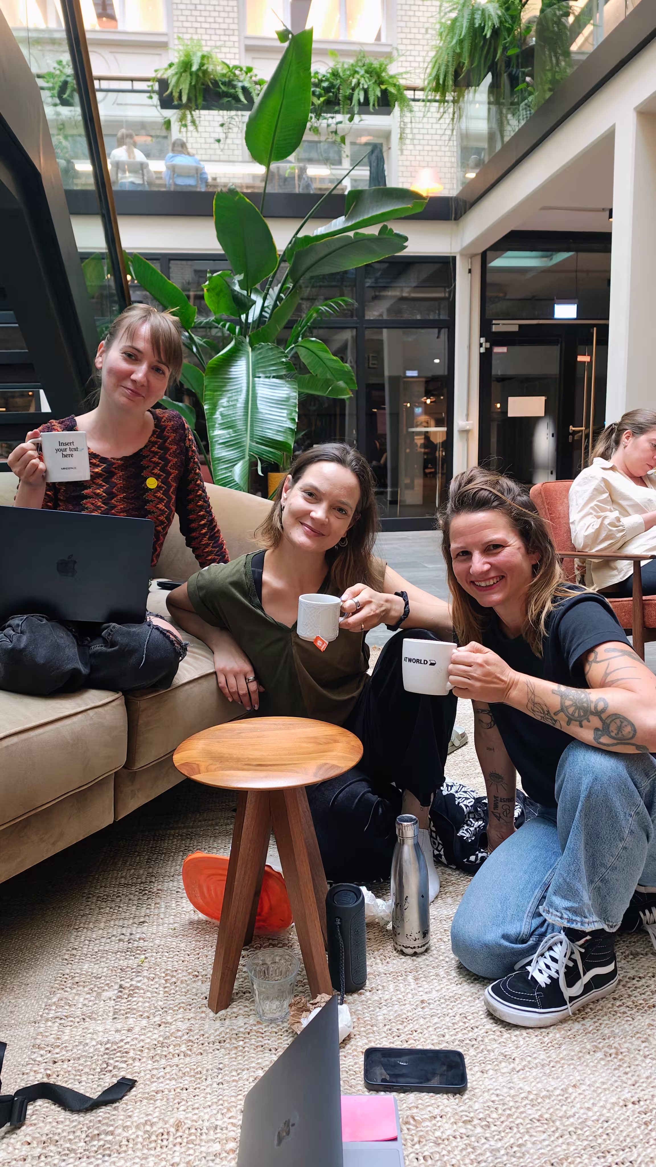 Magda and Verena and Marcelina smiling in co-working session, all holding white coffee mugs