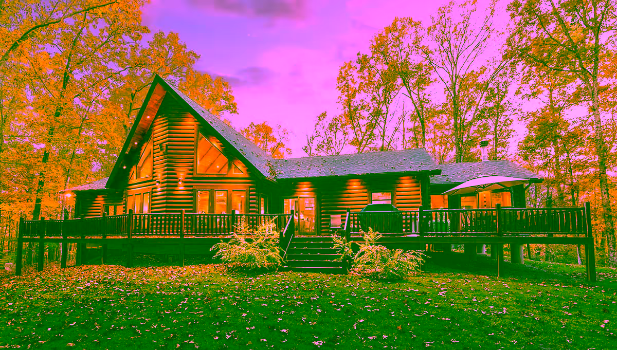 A log cabin home surrounded by autumn foliage, featuring large windows, a deck, and a staircase leading to the entrance. The warm colors of fall complement the wooden structure, creating a cozy atmosphere for custom homes and Amish homes.