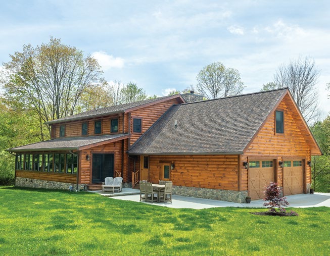 Levan custom log home in Howard, Ohio, featuring a long sunroom, stone foundation, outdoor patio, and attached two-car garage.