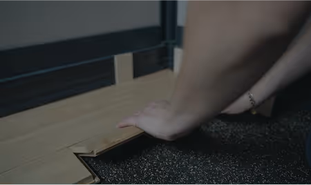 Une personne installe un parquet massif, l'image est assombrie