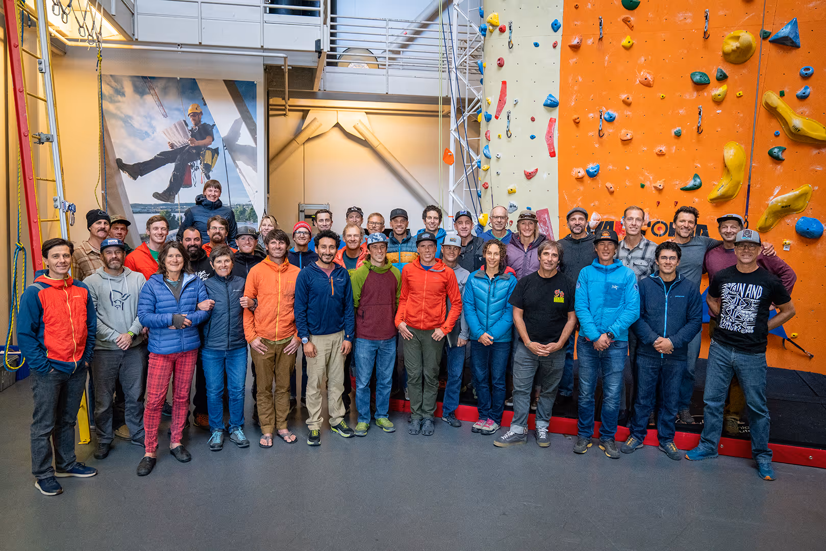 A group of people standing in front of an indoor rock-climbing wall, smiling at the camera.