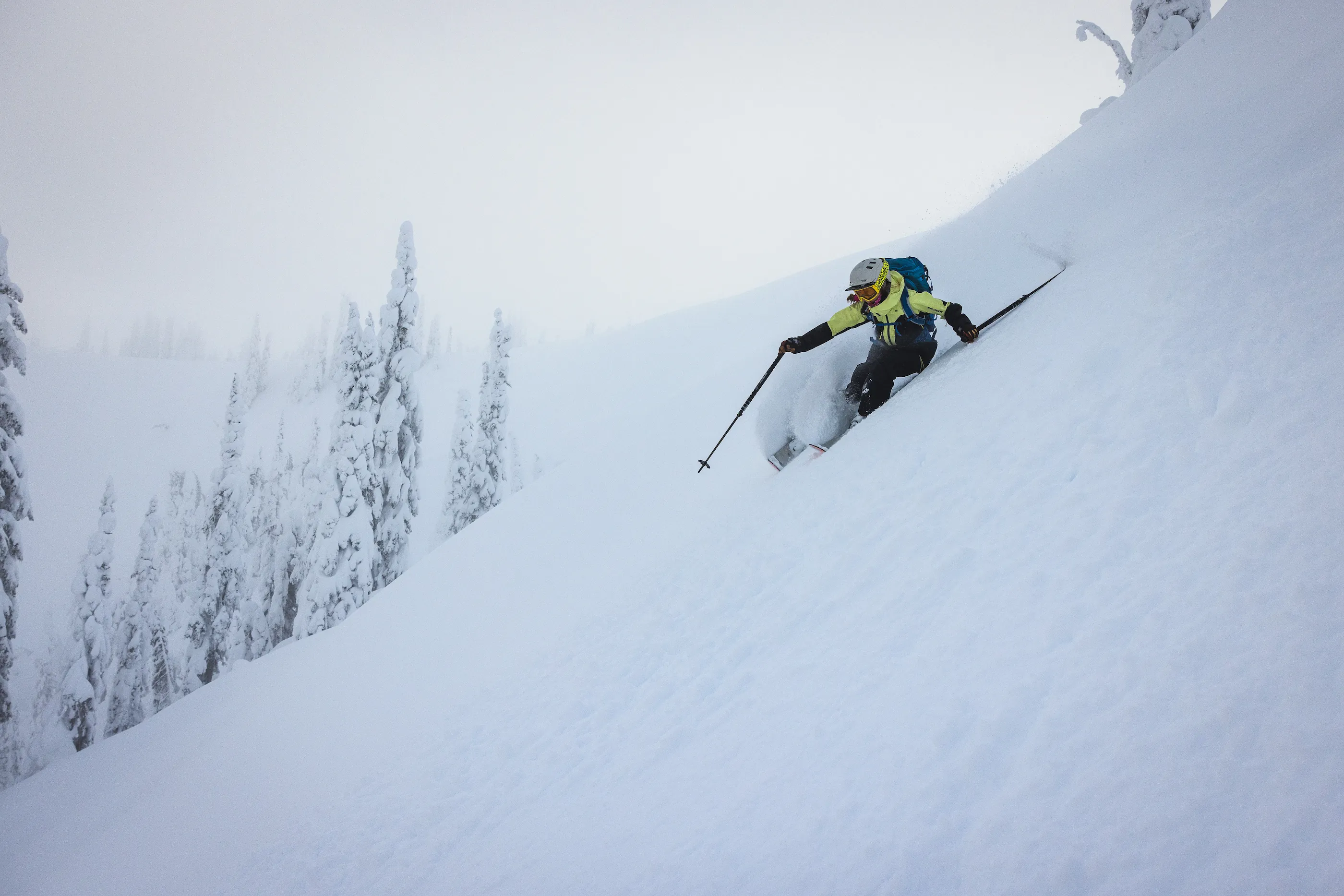 A person skiing down a snowy mountain slope with trees in the background.