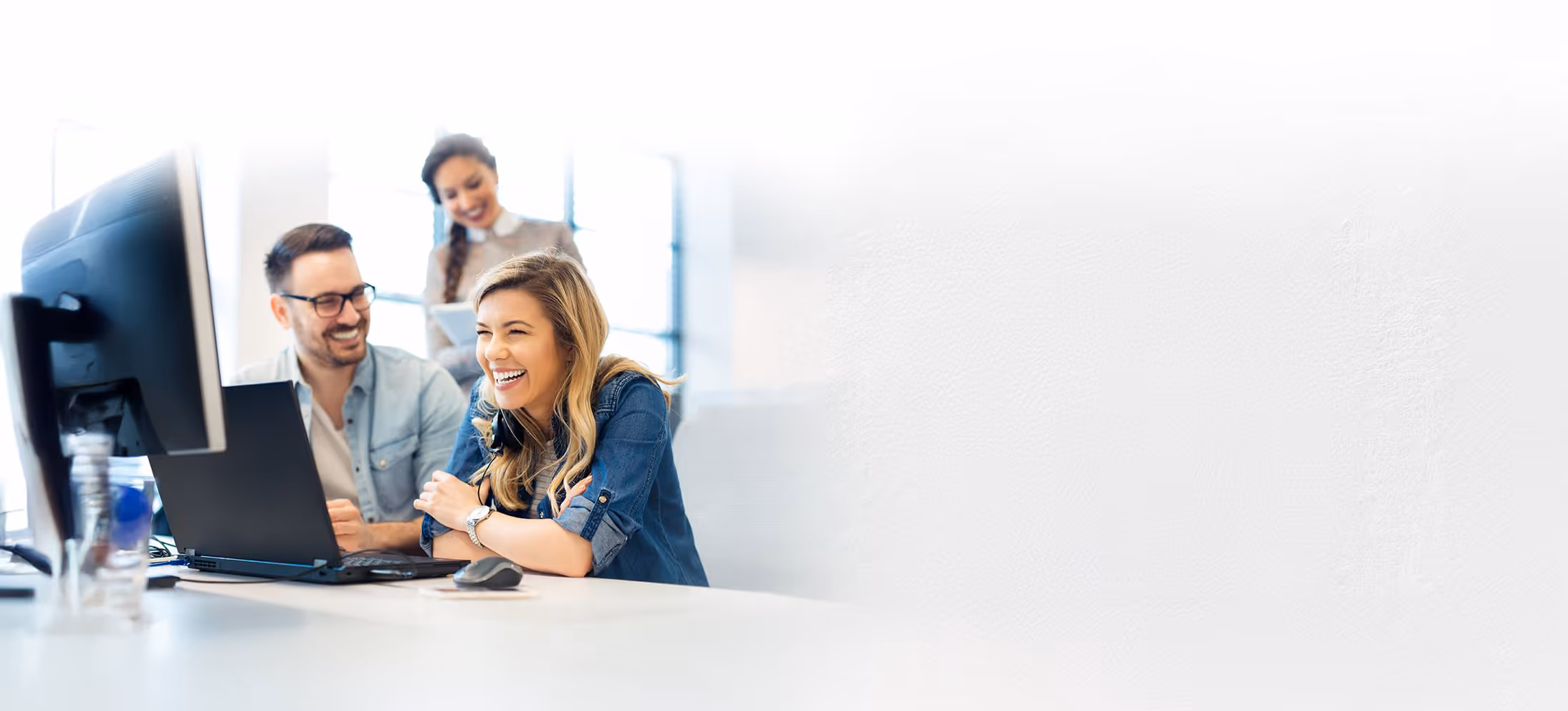 Two people smiling and working at a computer, with a third person standing in the background.