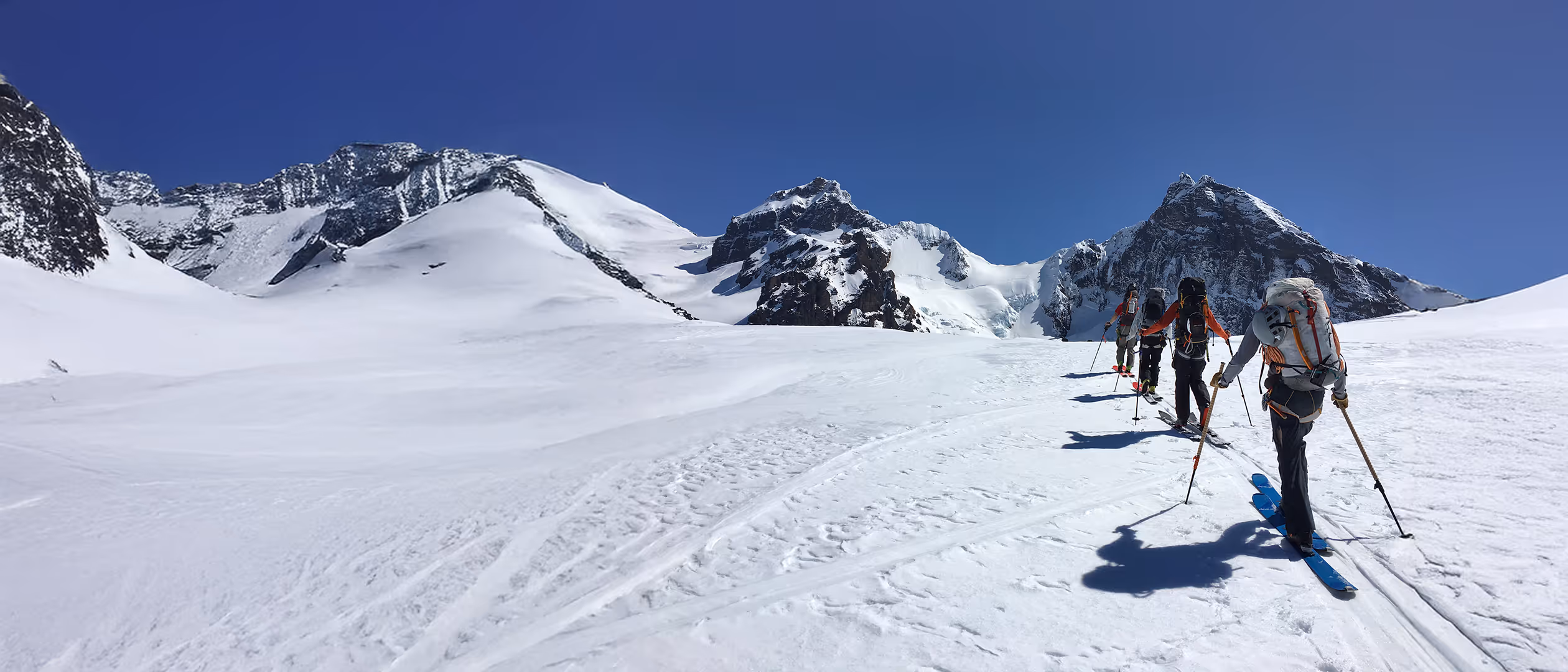 A group of skiers ascends a snowy mountain under a clear blue sky.