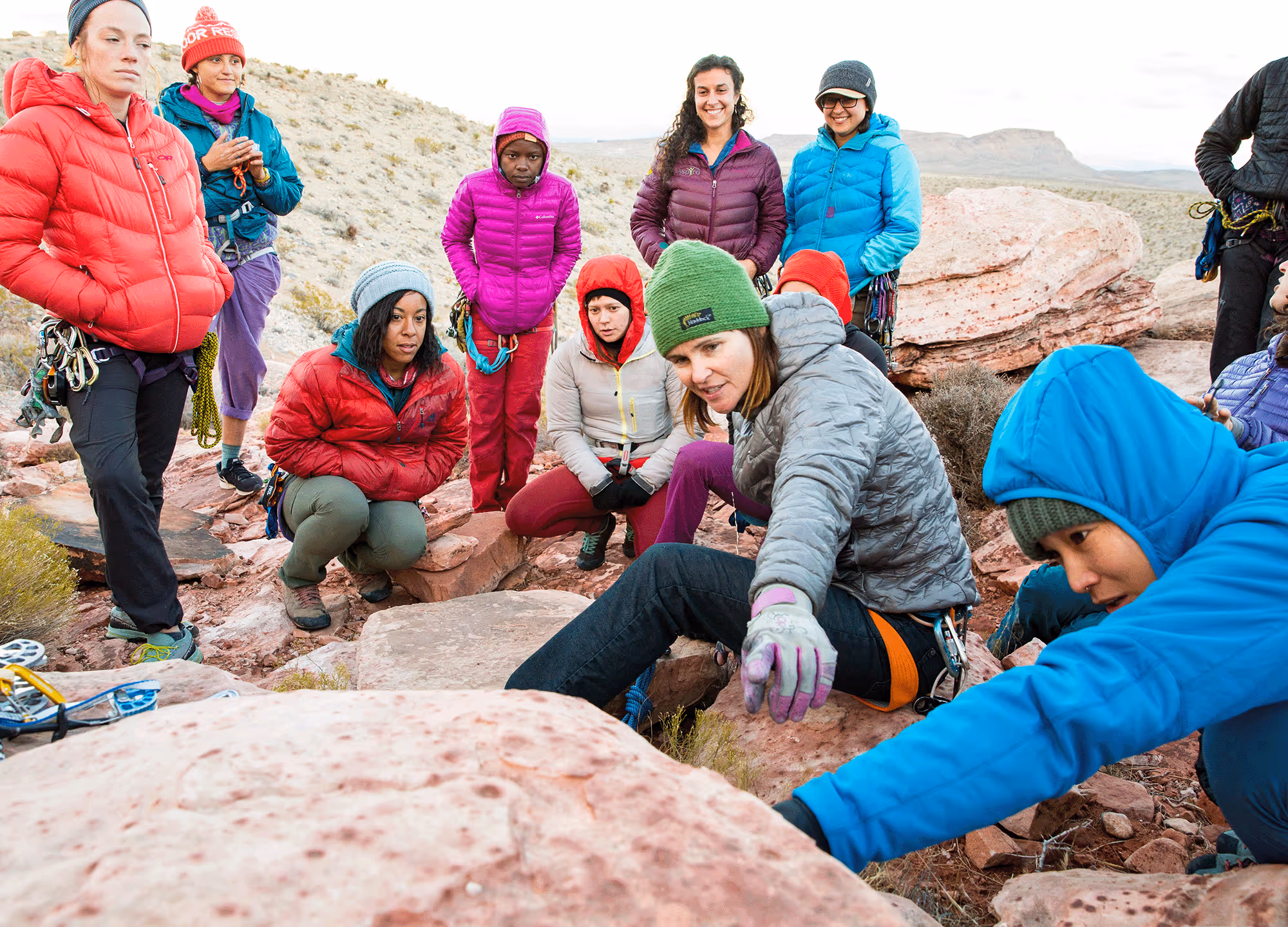 A group of people in warm clothing observe someone examining rocks in an outdoor setting.