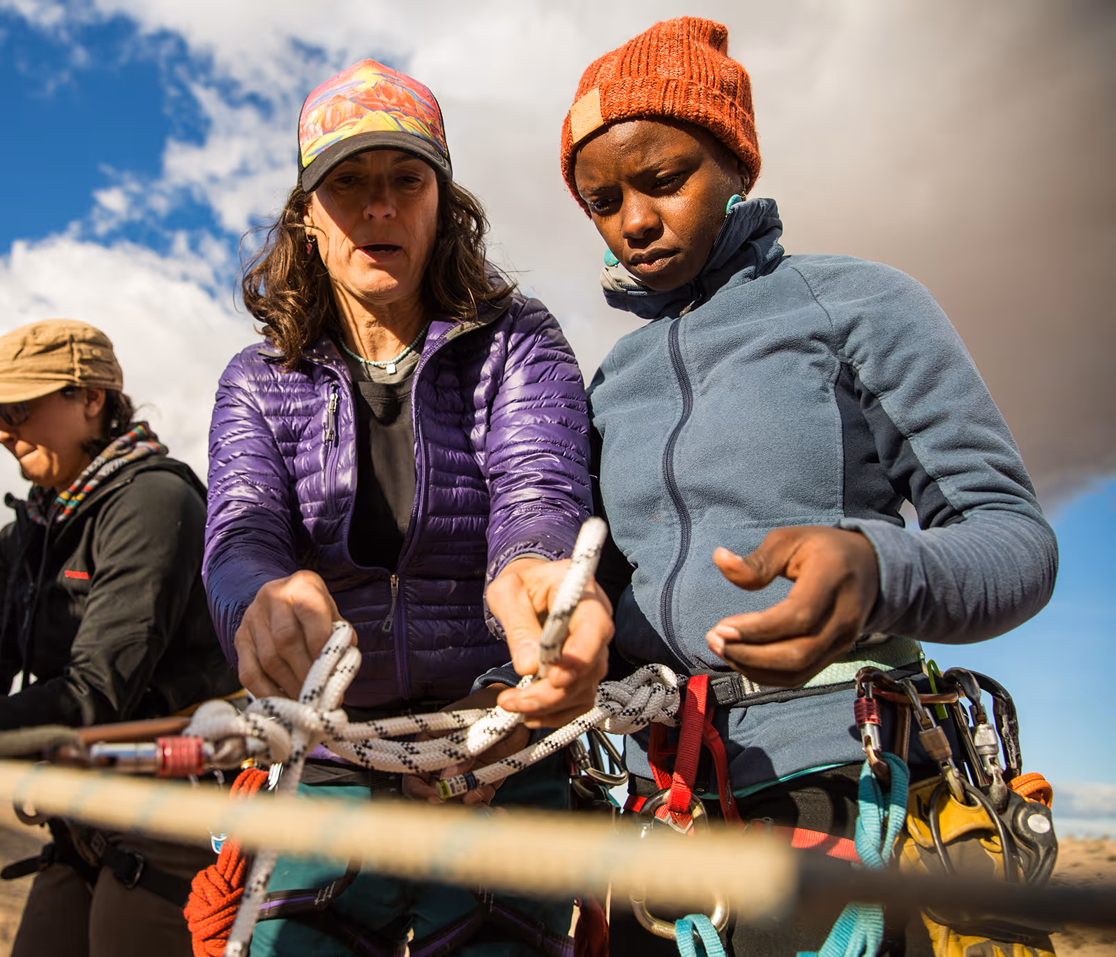 Two people work together to tie climbing ropes, wearing warm clothing and harnesses.