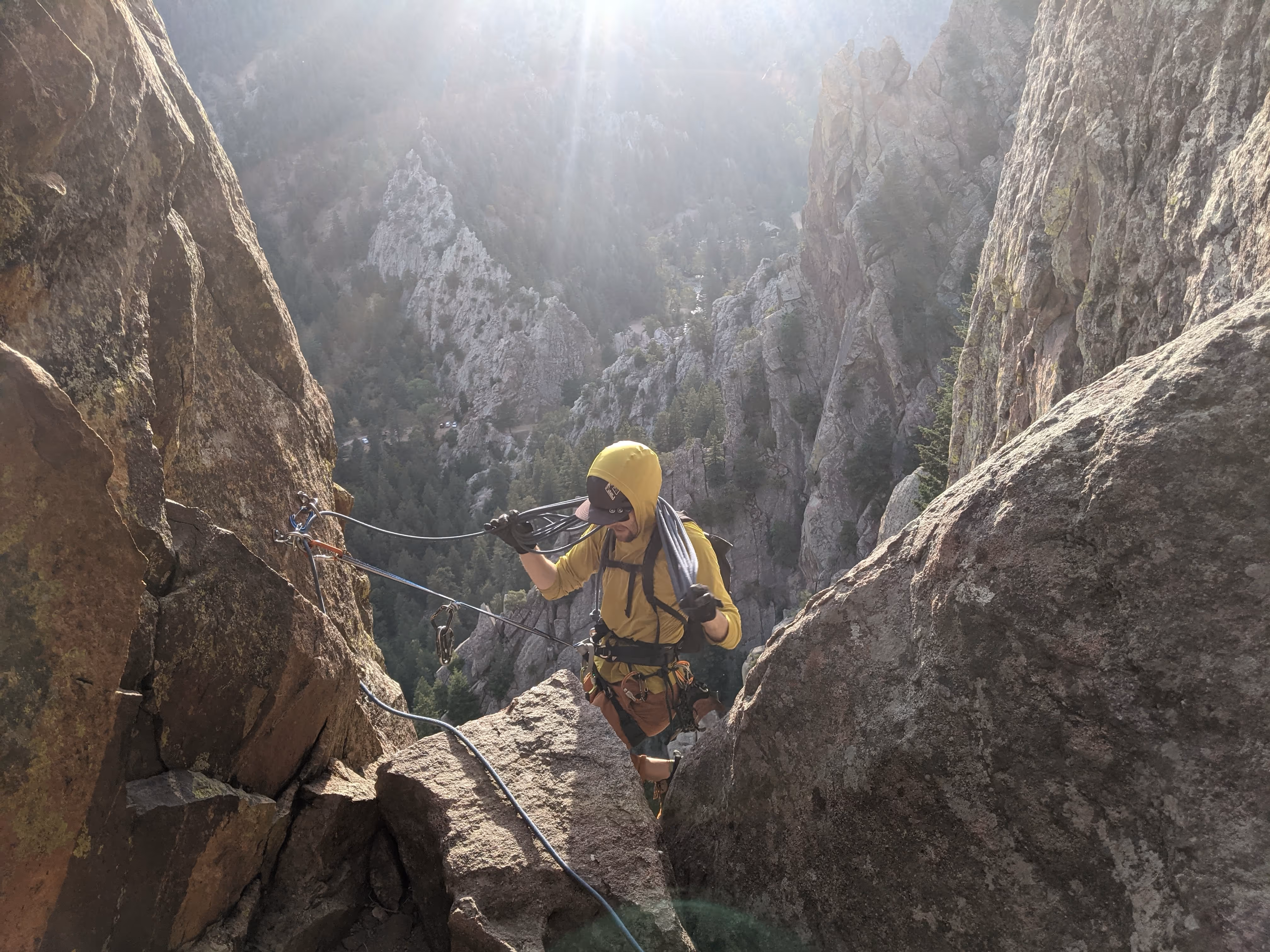A person in climbing gear ascends a rocky mountain path under bright sunlight.