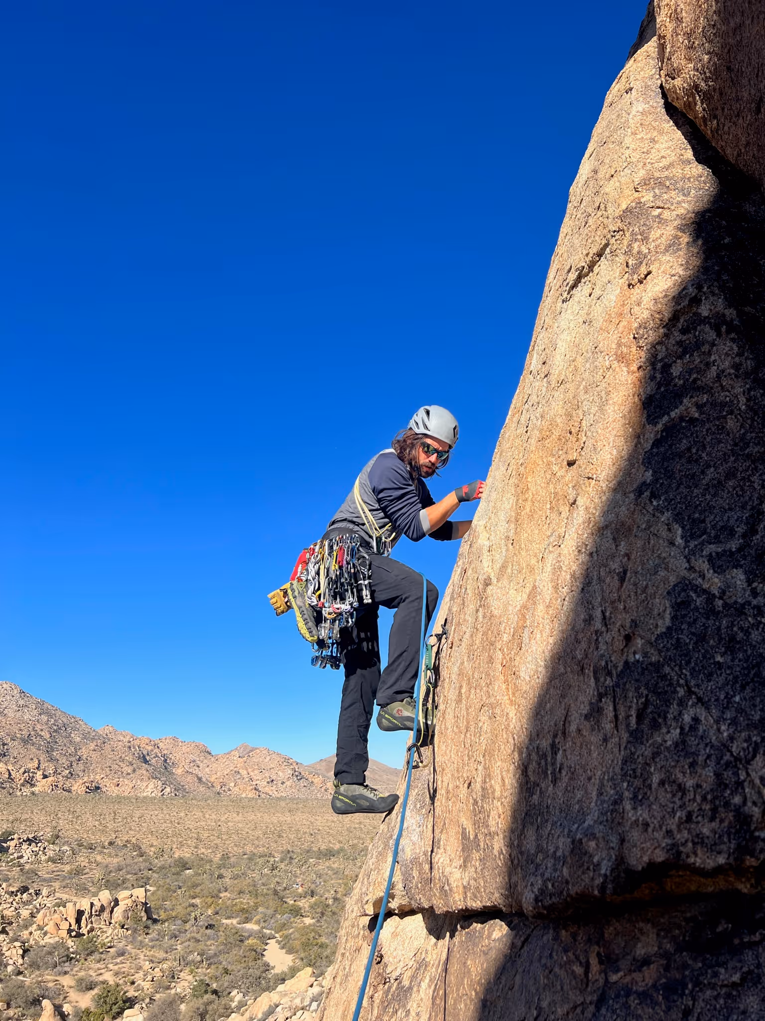 A person climbs a steep rock face, wearing a helmet and carrying climbing gear.