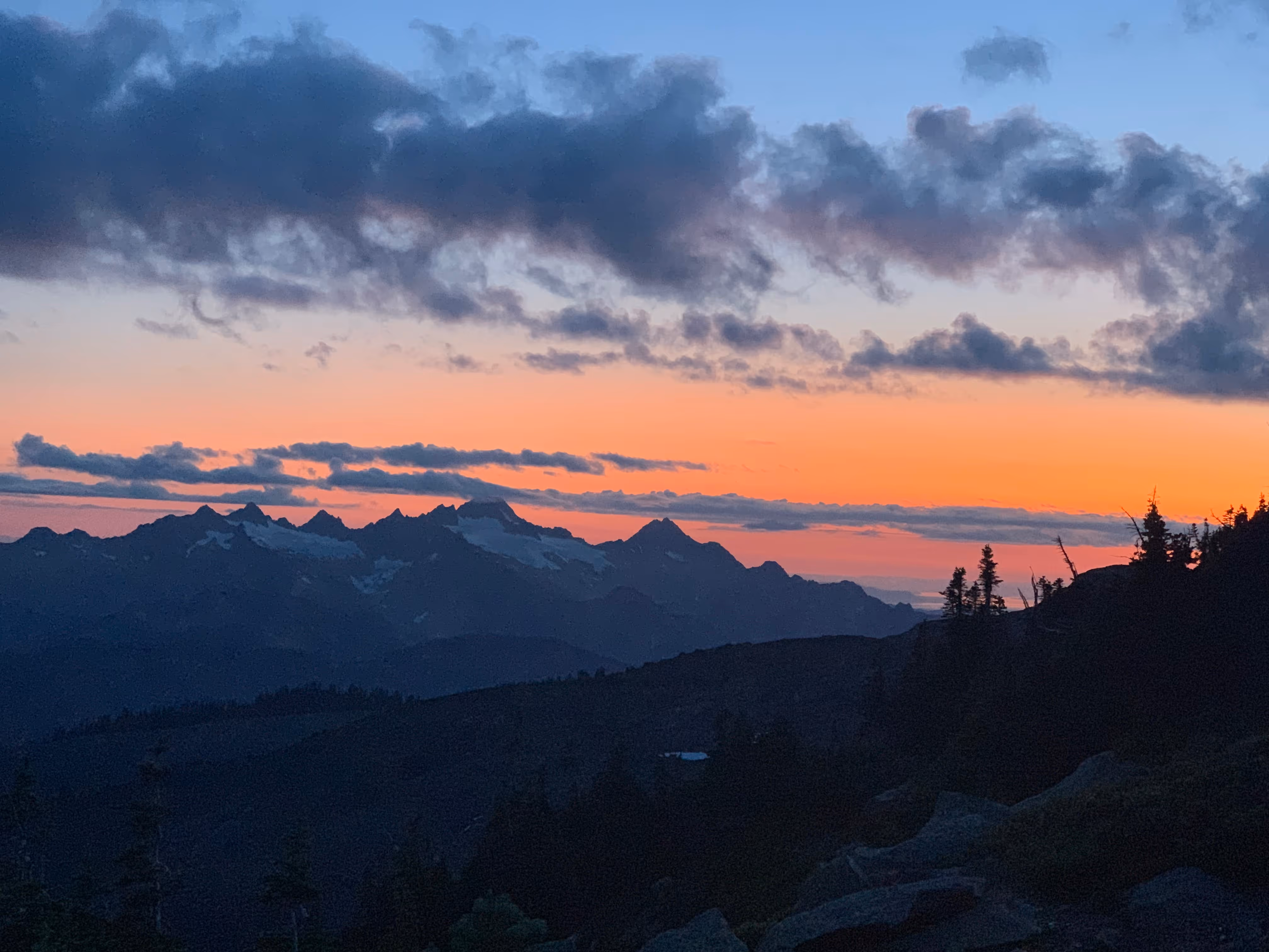 Mountain range at sunset with a colorful sky and scattered clouds.