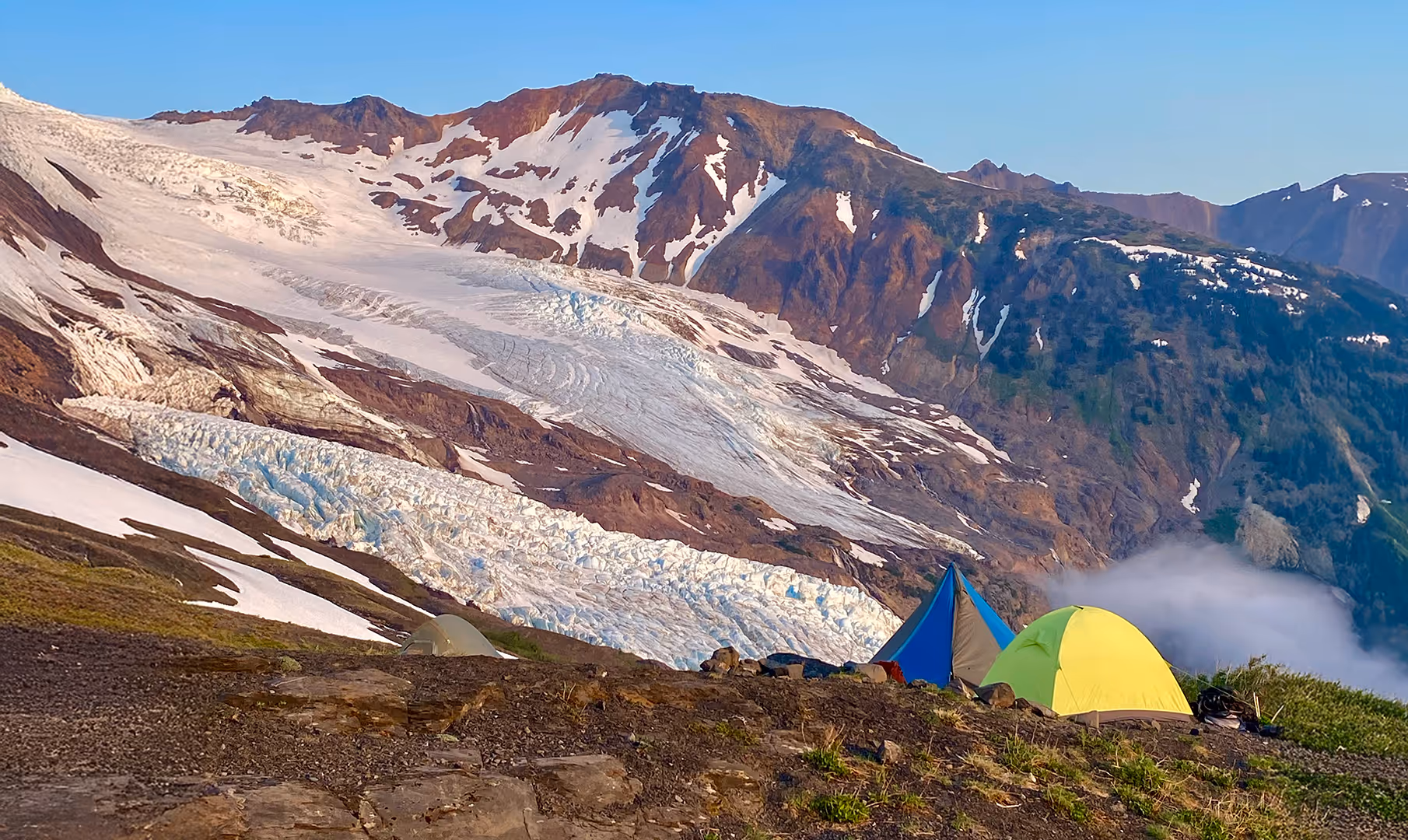Two tents set up on a grassy hill in front of a snowy mountain landscape.