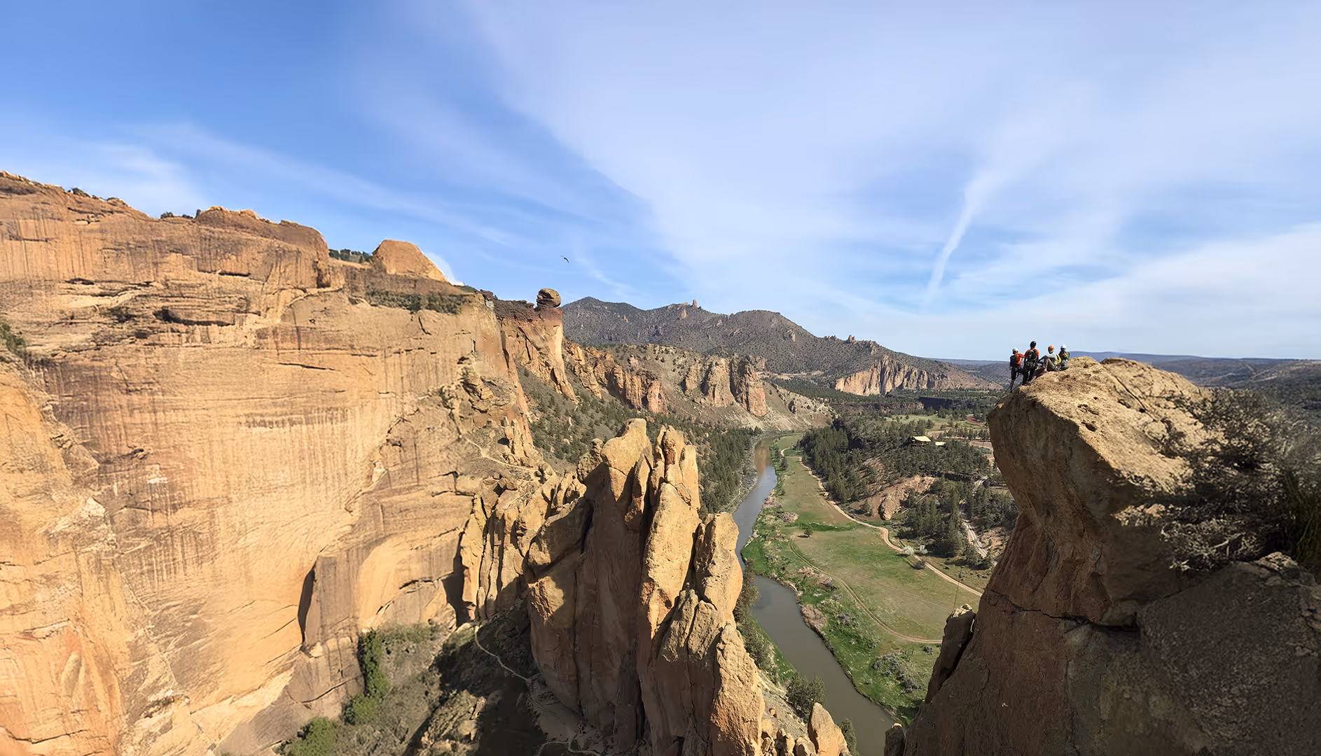 People stand on a cliff edge overlooking a wide canyon with a river below.