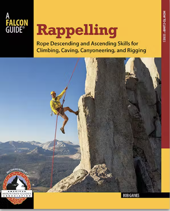 A person rappels down a rock face with mountains visible in the background.