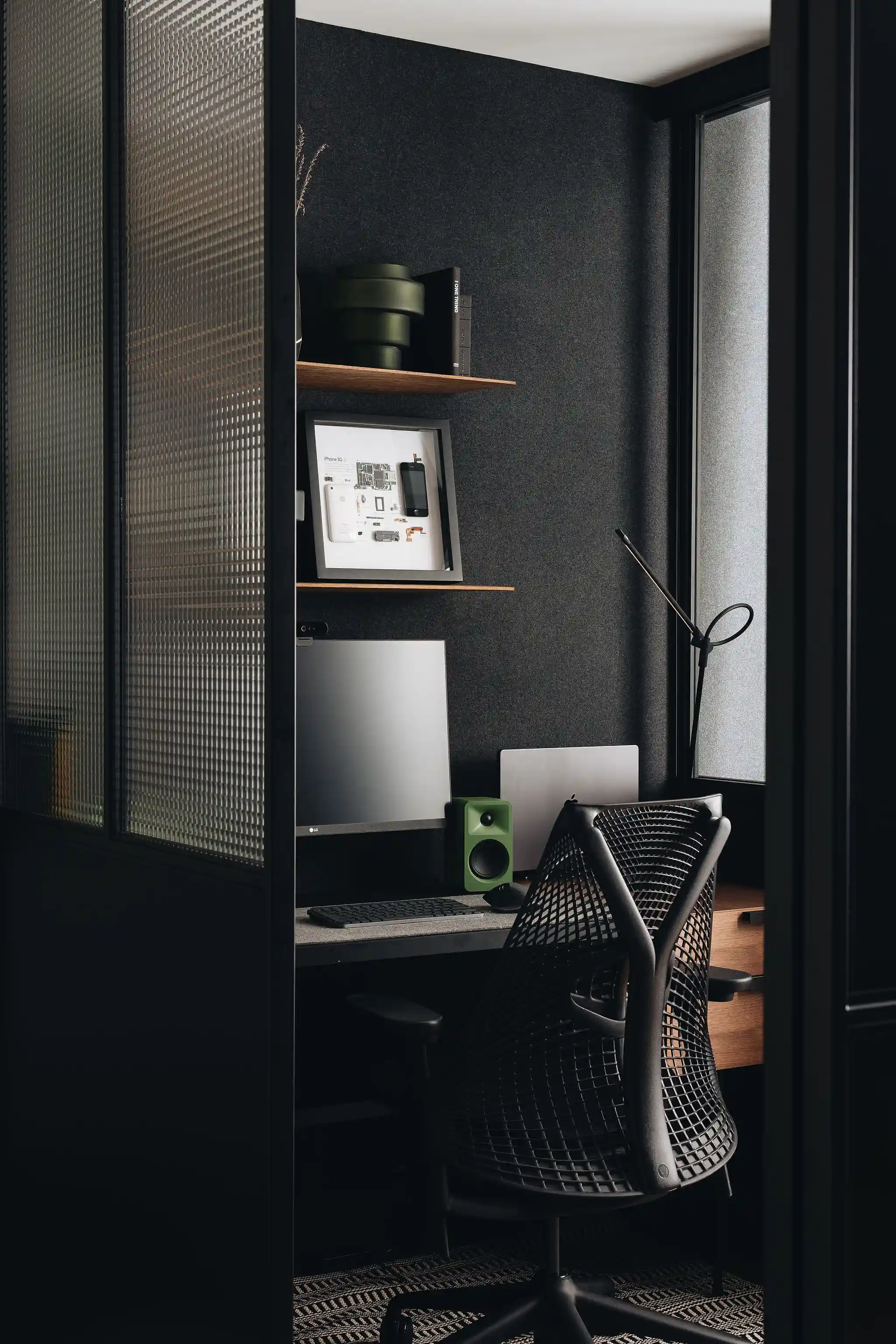 Cloison vitrée en verre cannelé séparant un bureau sombre avec mur acoustique et fauteuil ergonomique, projet Baril