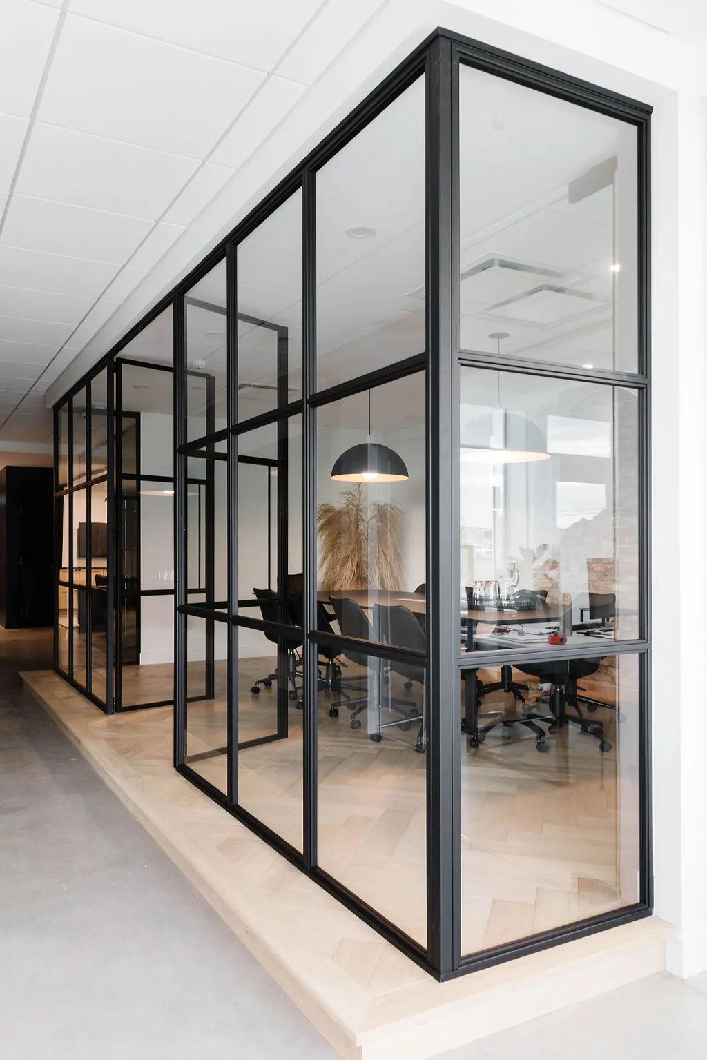 Cloison vitrée de style atelier noire fermant une salle de réunion avec parquet chevron et grandes baies vitrées, projet CMPG