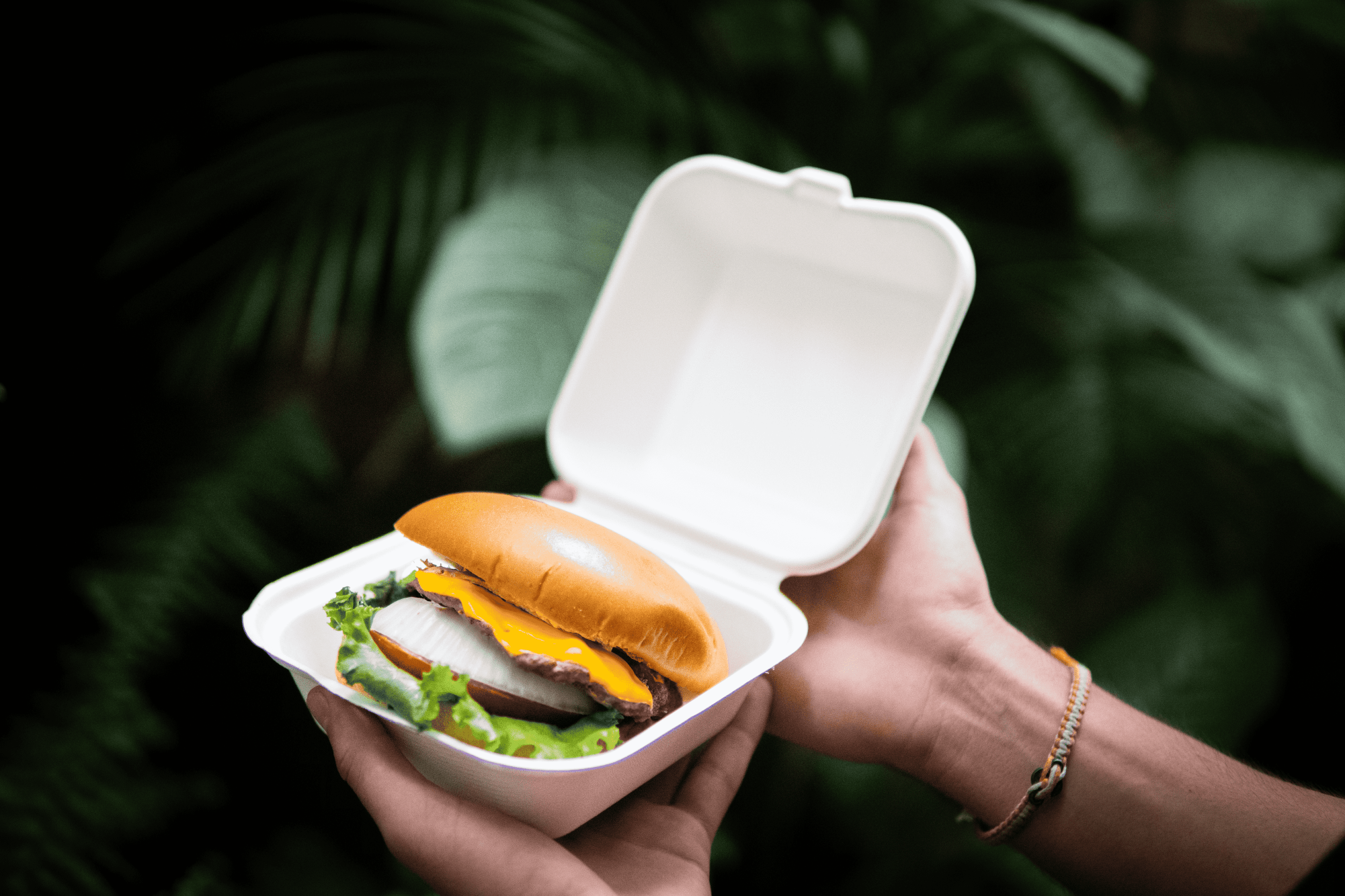 2 manos sosteniendo un contenedor de comida con una hamburguesa