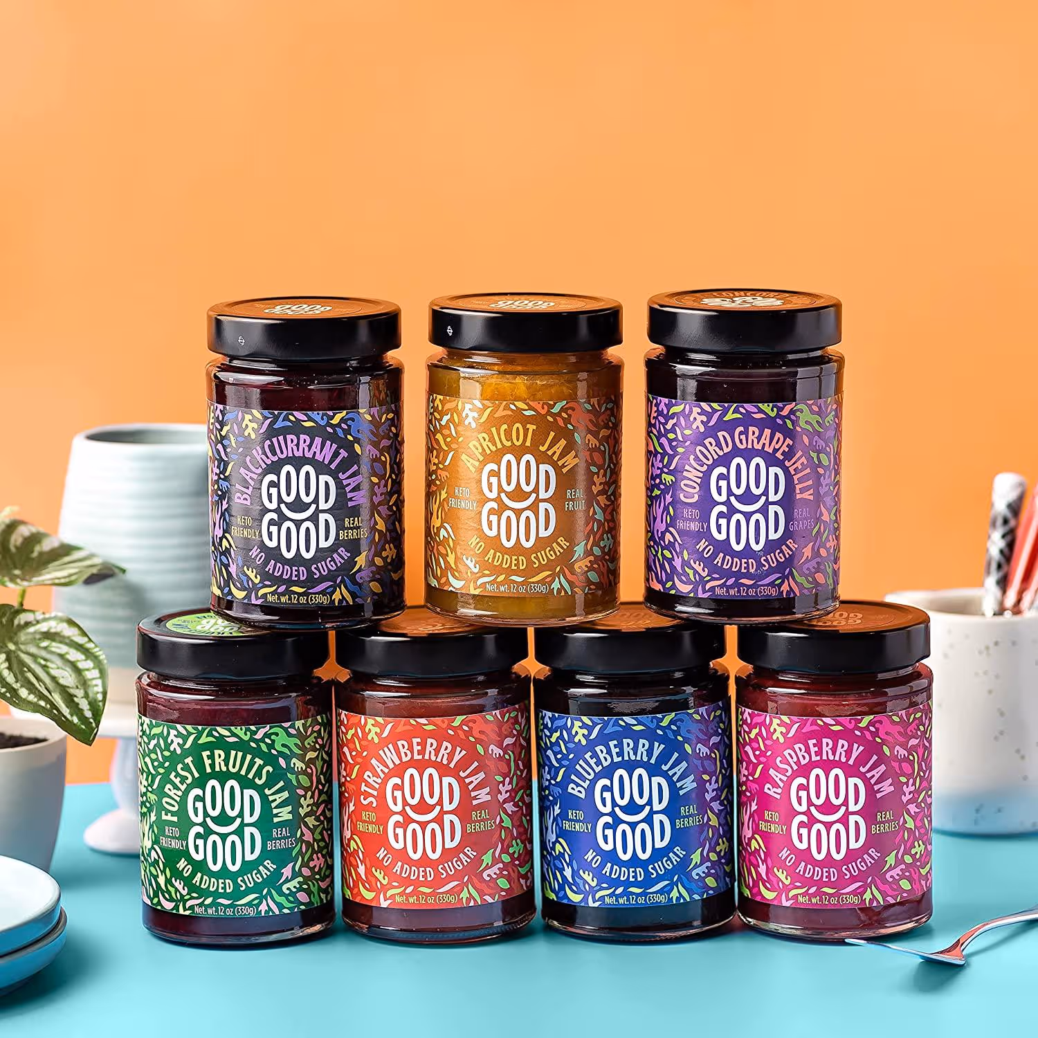 Seven jars of Good Good no added sugar jams arranged in two rows, featuring blackcurrant, apricot, concord grape, forest fruits, strawberry, blueberry, and raspberry flavors