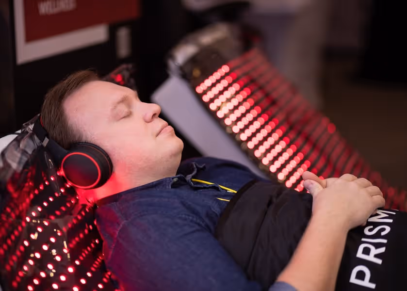 Person lying down receiving red light therapy with LED panel, wearing headphones during wellness treatment