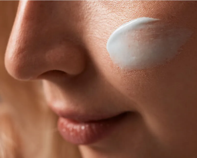 Close-up of a person's cheek with a dollop of white cream applied.