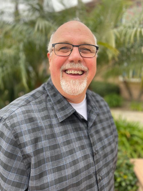 A man smiling in front of greenery
