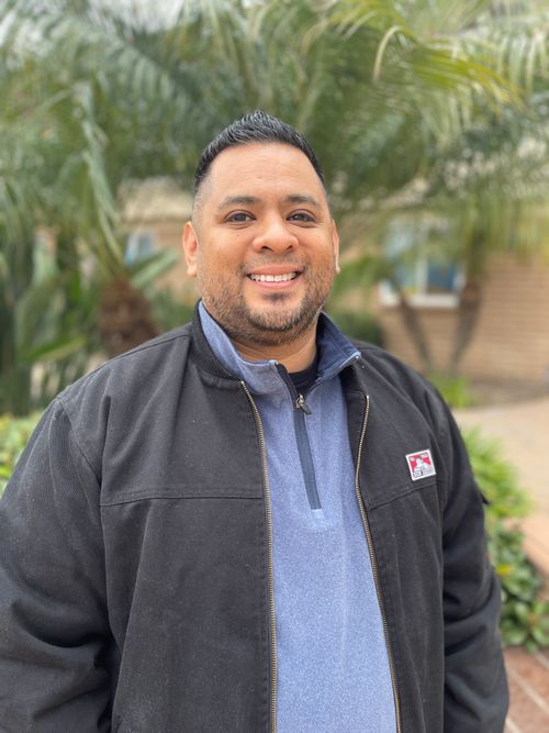 A man smiling in front of greenery