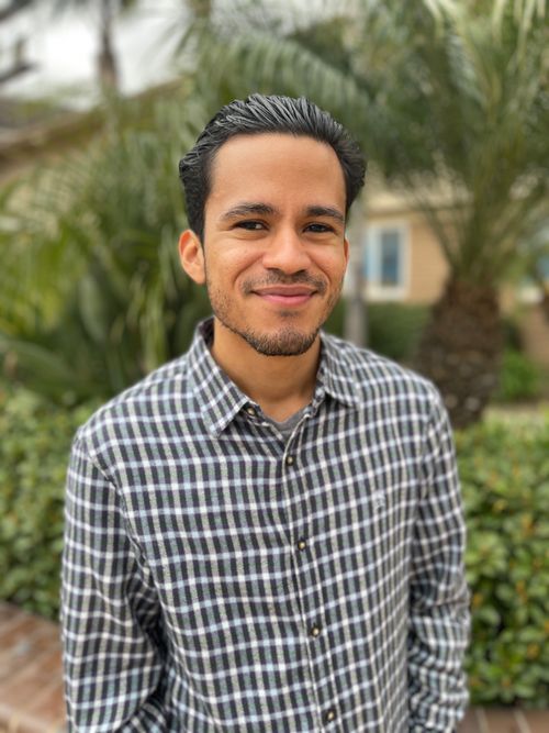 A man smiling in front of greenery