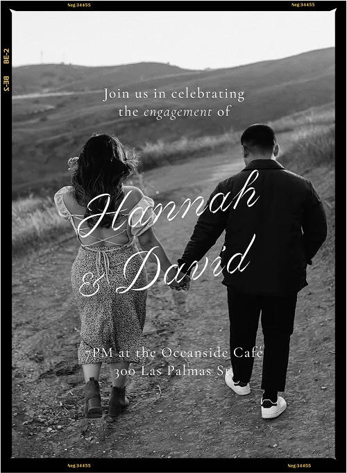 Black and white photo of a couple holding hands walking on a dirt path in a hilly landscape.