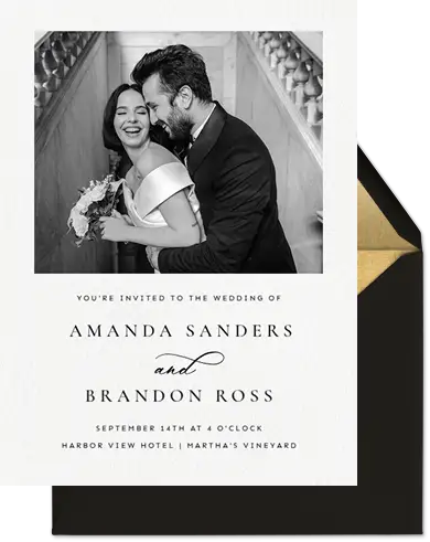 Black and white wedding invitation with a smiling bride and groom embracing on stairs.