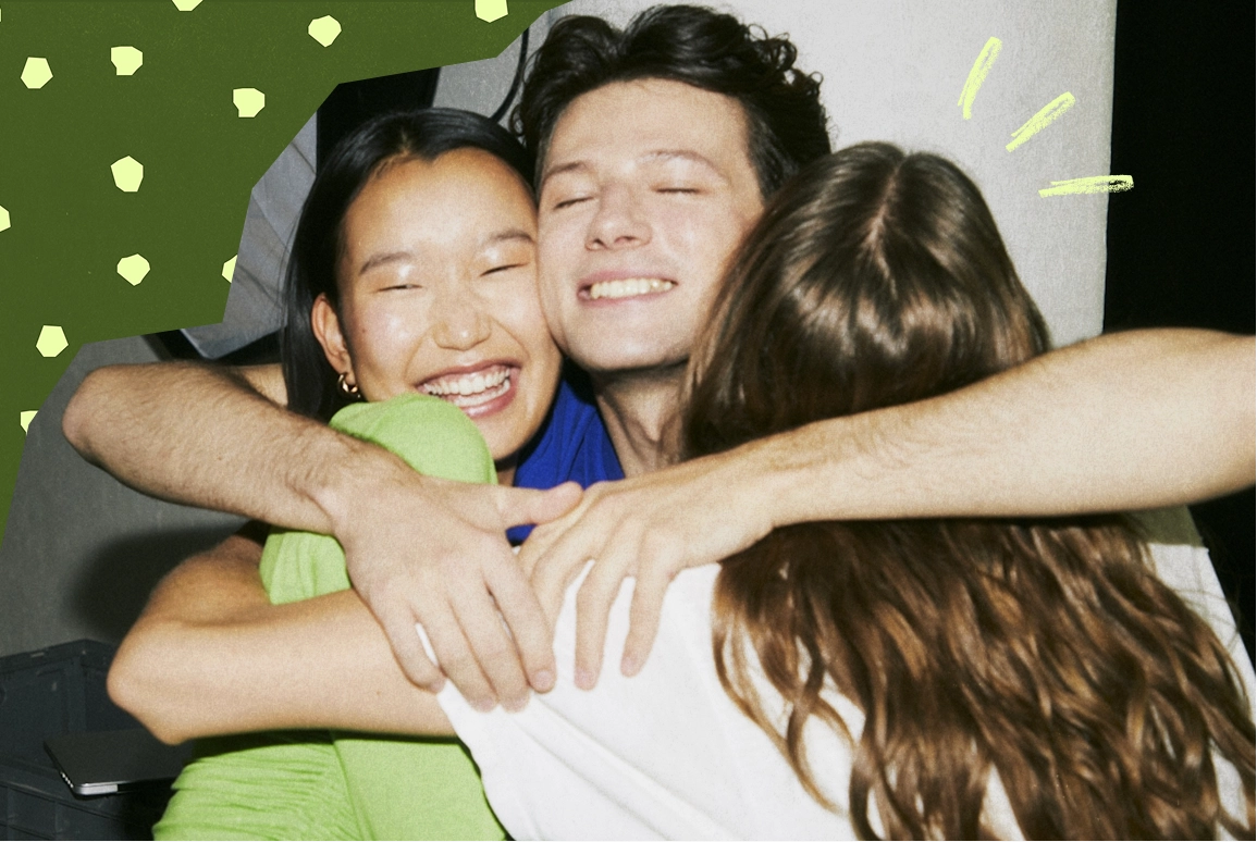 Three friends smiling and hugging each other closely in a joyful group embrace.