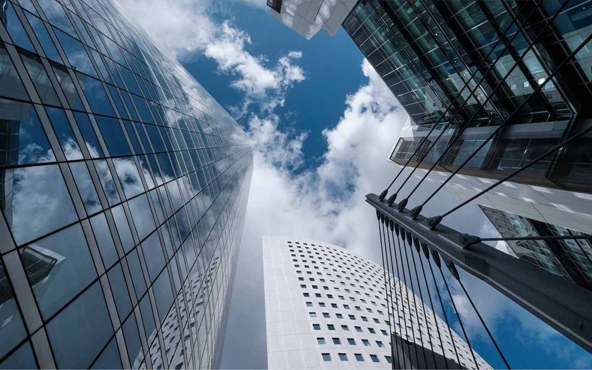 Upward view of modern skyscrapers with reflective glass windows and a partly cloudy blue sky.