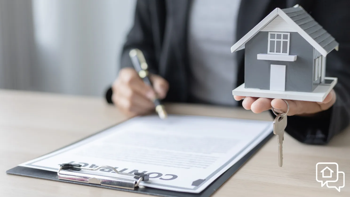 Agente inmobiliario sosteniendo una maqueta de vivienda y llaves sobre un contrato de compraventa