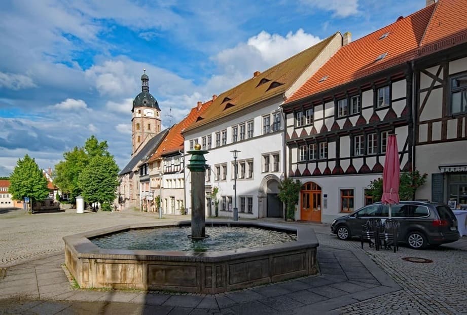 Marktplatz mit Brunnen, Fachwerkhäusern und Kirchturm bei blauem Himmel in einer Stadt in Sachsen-Anhalt