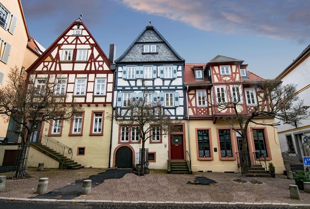 Drei historische Fachwerkhäuser mit farblich abgesetzten Holzstrukturen in Rot, Blau und Braun.