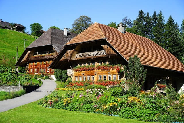 Traditionelle Einhöfe mit Holzfassade und üppigem Blumenschmuck in idyllischer Hanglage.