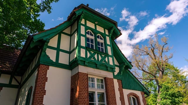 Zweigeschossiges Haus mit roter Backsteinfassade im unteren Bereich und grün gestrichenem Fachwerk im Giebel.
