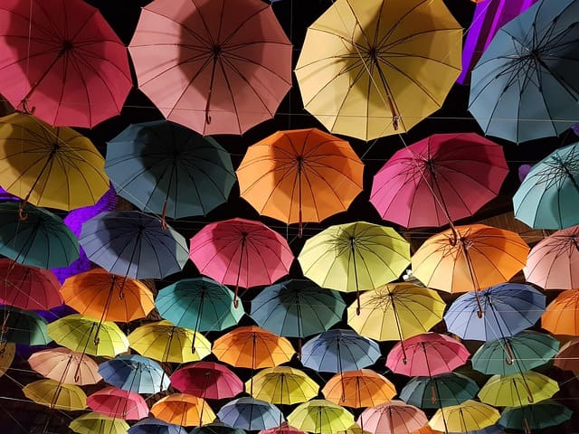 Viele bunte Regenschirme hängen in Reihen über einer Straße und bilden ein farbenfrohes Dach.