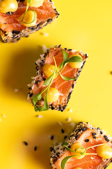 Tataki de saumon avec graines de sésame, mayonnaise et herbes vertes sur fond jaune.