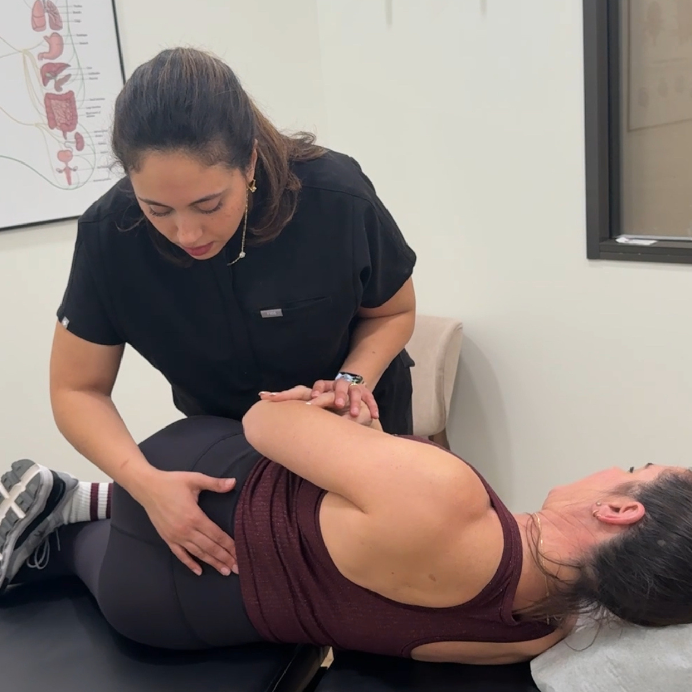 Physical therapist assists patient with spine stretch on a treatment table in a clinic room.