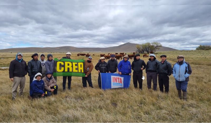 A group of farmers standing in grassland holding CREA and INTA banners, with cattle and hills behind