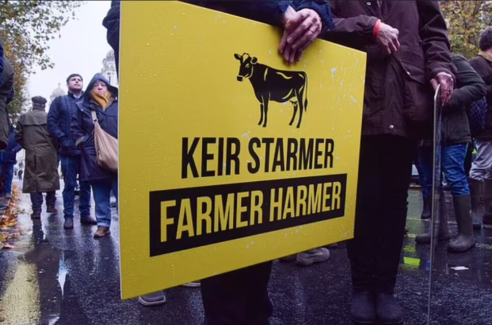 A yellow placard reading Keir Starmer Farmer Harmer held at a protest on a wet street