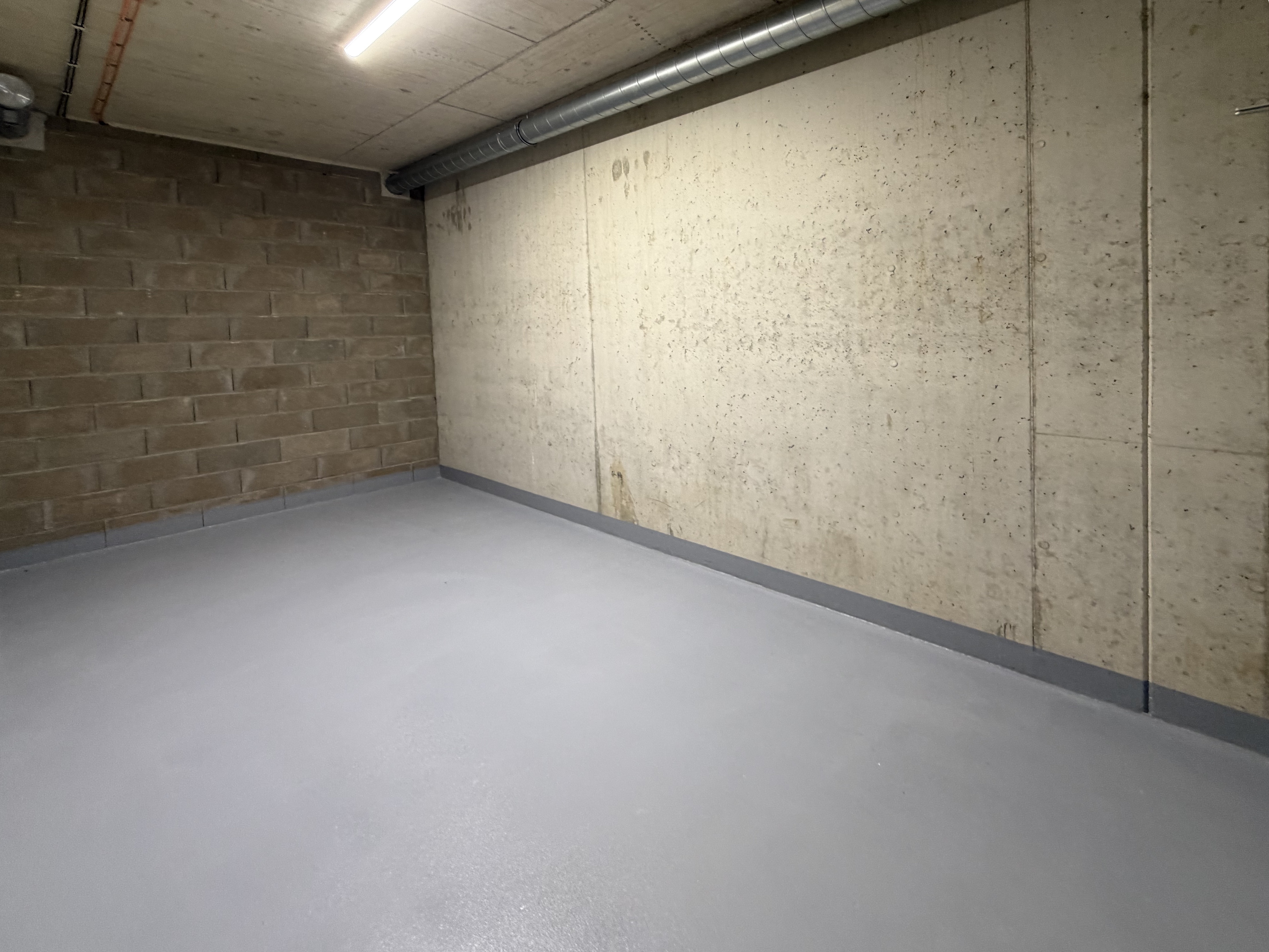Prázdná betonová místnost s cihelnou a betonovou stěnou a šedou podlahou pod stropním světlem.