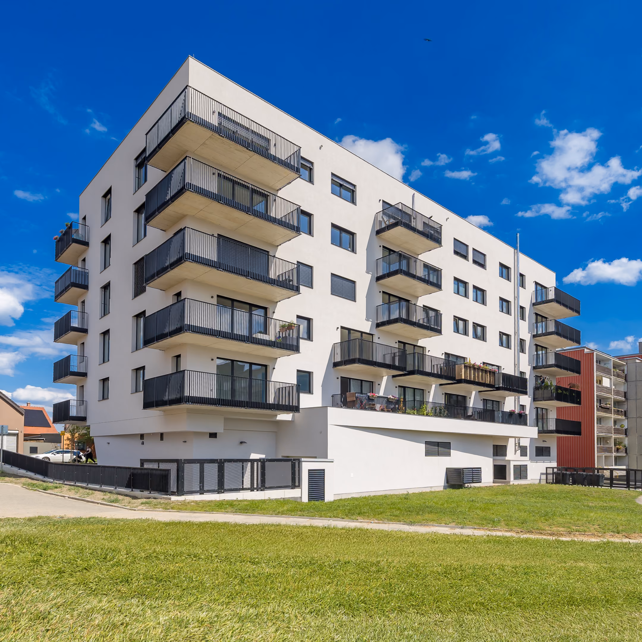 Moderní ložnice s velkou postelí se šedým čalouněním, bílým povlečením a žlutými polštáři, nočními stolky a oknem.