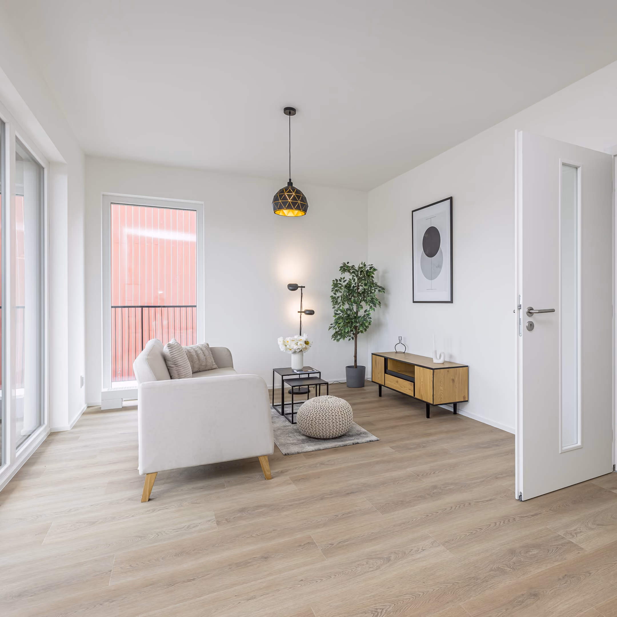 Moderní obývací pokoj s bílou pohovkou, dřevěnou skříňkou, rostlinou a závěsným osvětlením.