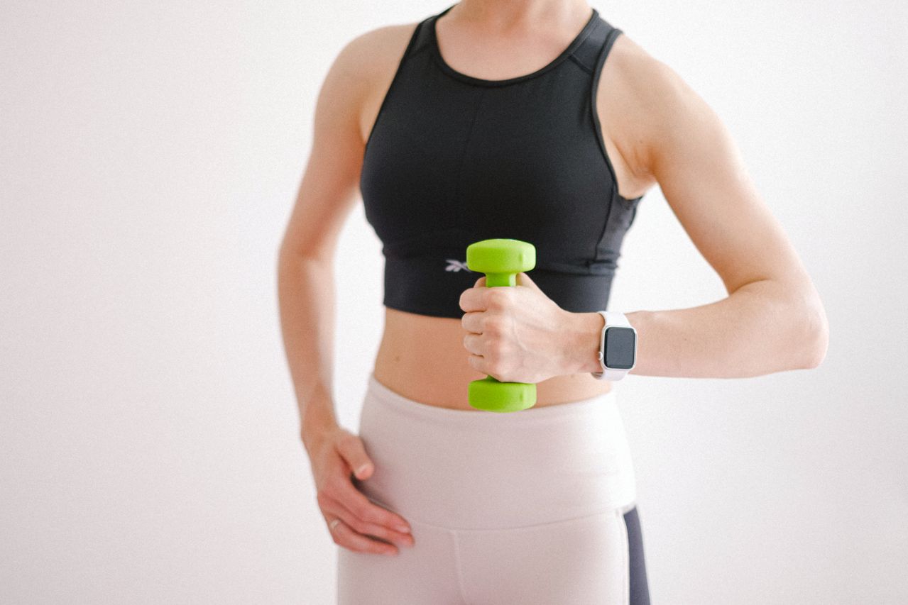 fit woman holding green dumbbell with smartwatch on white background
